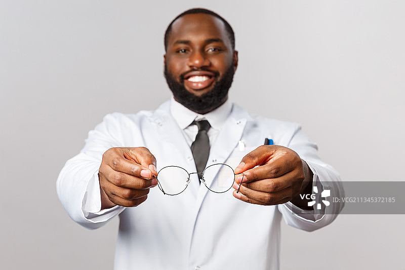 面带微笑的男子拿着眼镜站在灰色背景前的肖像照图片素材