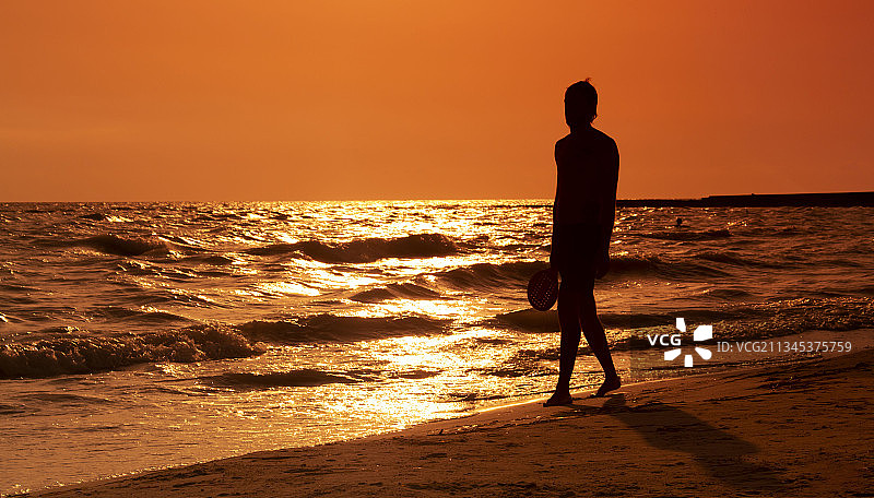 日落时分站在意大利里窝那省滨海滩边的男子轮廓图片素材