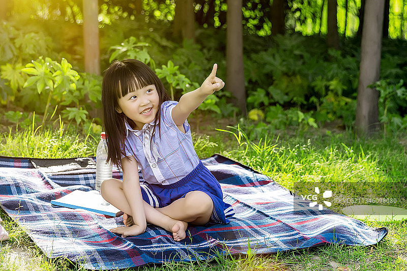 周末小女孩坐在公园草地上手指前方图片素材