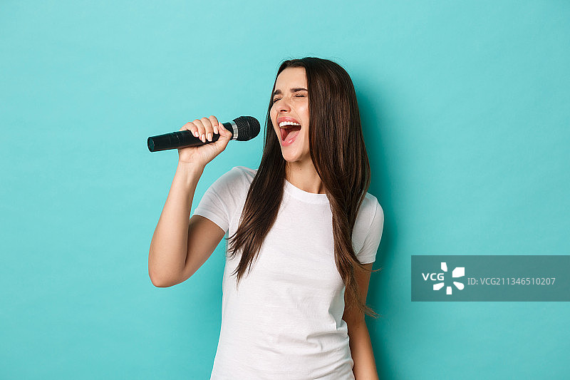 年轻女人站在蓝色背景前唱歌图片素材