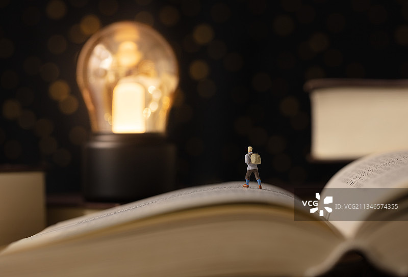 微缩创意书本上的灯泡照亮前行的旅行者图片素材