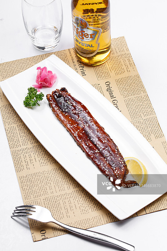 长方形瓷盘装的日式烤鳗鱼摆放在英文包装纸上图片素材