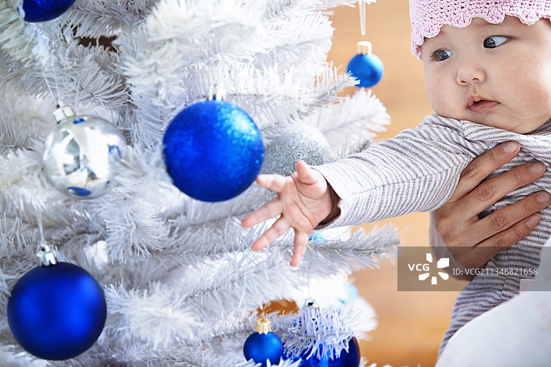 一岁大的孩子在妈妈的怀里看着圣诞树和装饰品图片素材