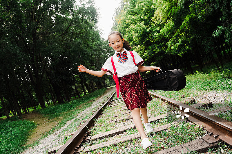 小学生提着小提琴盒在铁轨上走图片素材