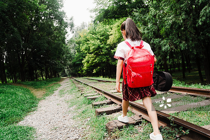 小学生提着小提琴盒在铁轨上走图片素材