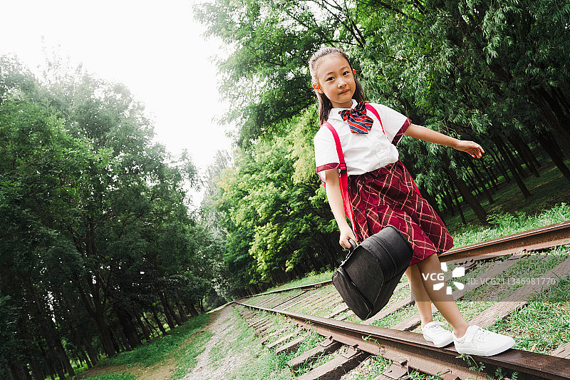 小学生提着小提琴盒在铁轨上走图片素材