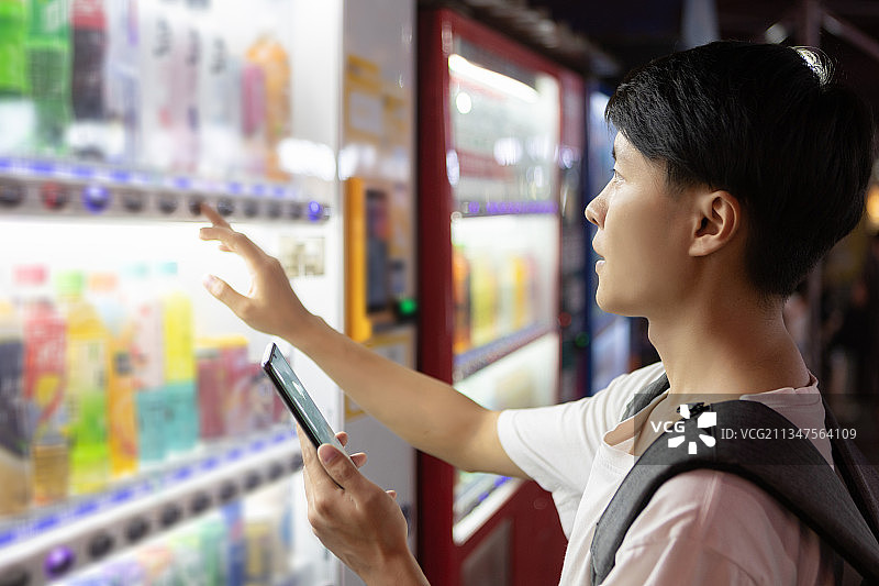 亚洲男性青年在城市里使用手机购买无人售货贩卖机图片素材