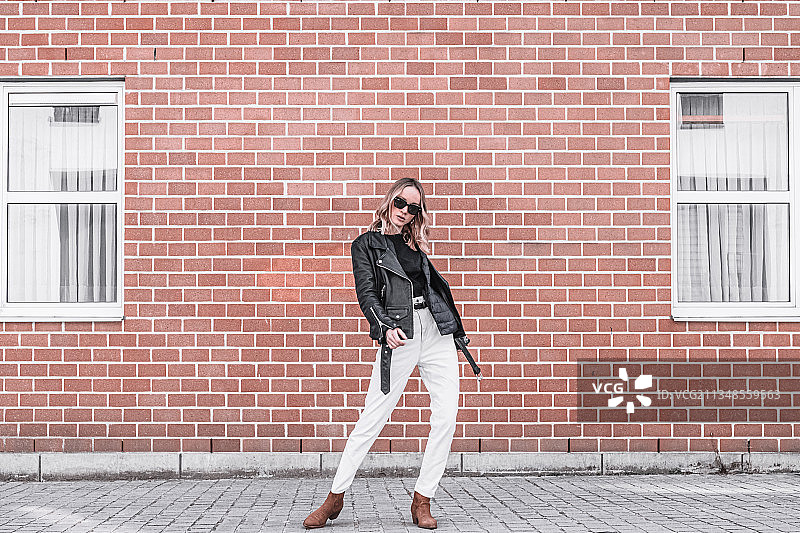 站在砖墙前的戴太阳镜的年轻女子肖像，比利时安特卫普图片素材