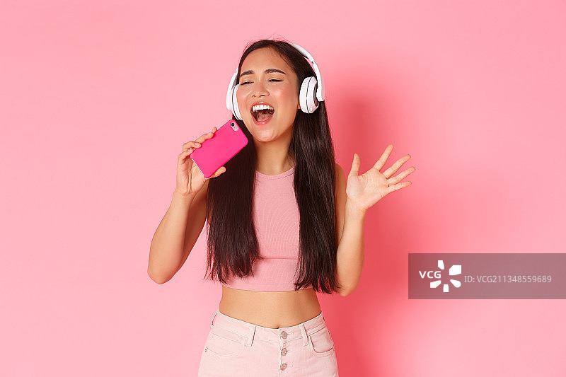 快乐的年轻女子在粉红色背景下听音乐图片素材