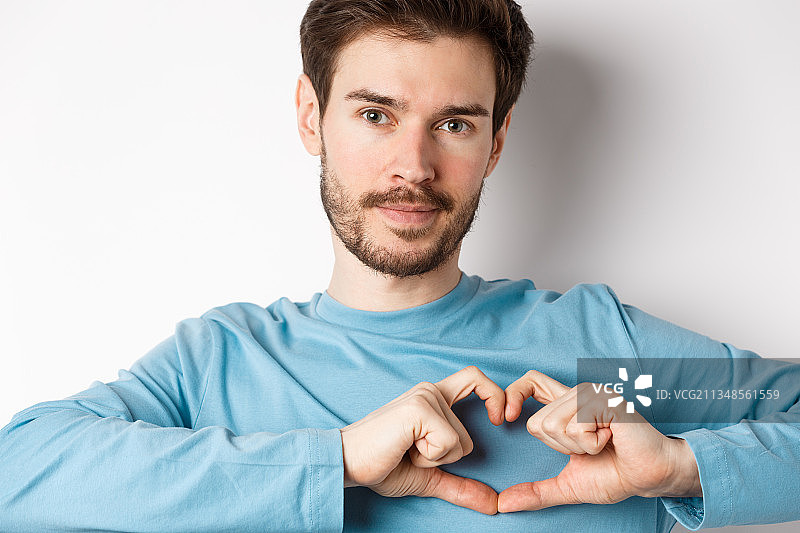 在白色背景前用手比心的年轻男人肖像图片素材