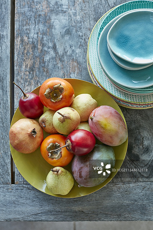 户外桌子上摆放的油金芒、芒果、柿子、梨和彩色盘子的水果拼盘图片素材