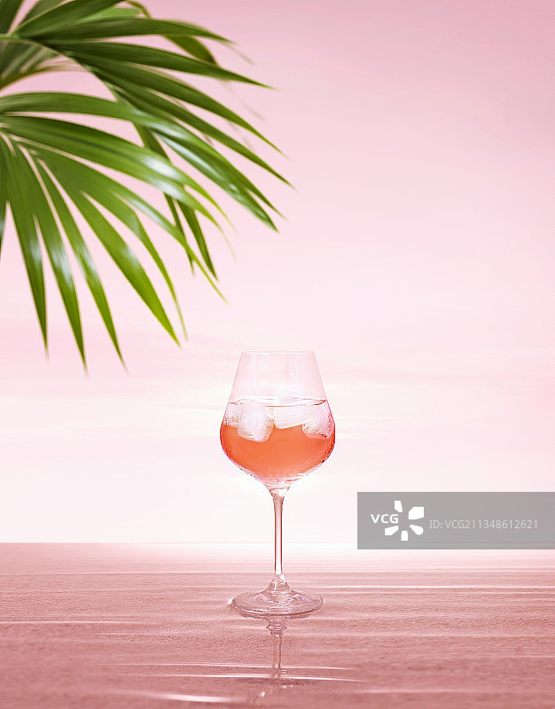 粉色水面天空日落下的冰镇玫瑰葡萄酒，配两片棕榈叶图片素材