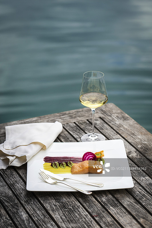 烤盘和一杯白葡萄酒，在木桌上享用，可欣赏湖景图片素材