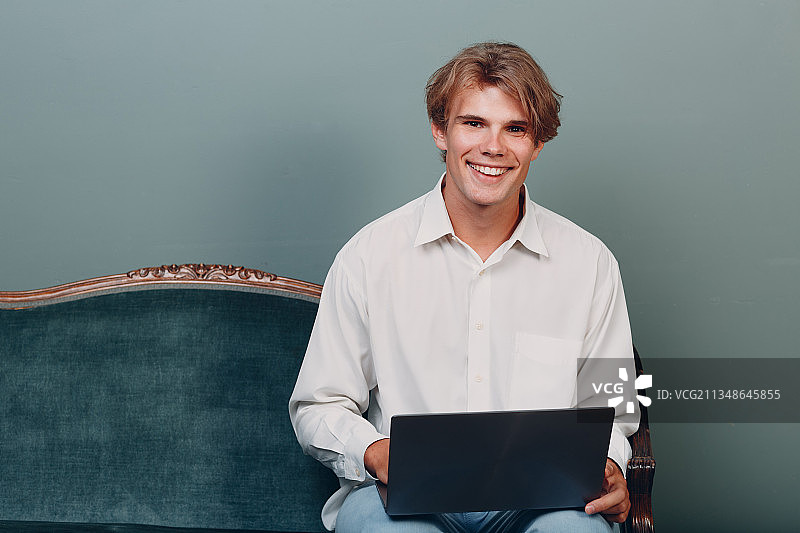在沙发上使用笔记本电脑的微笑男人图片素材