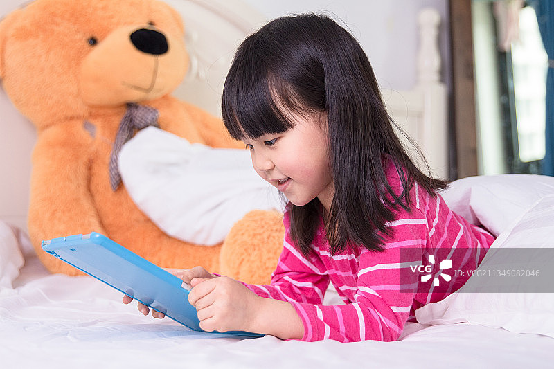 趴在床上看平板电脑的小女孩图片素材