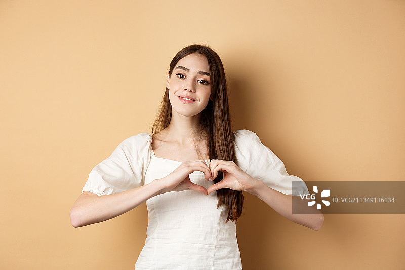 年轻女人在米色背景前做心形手势图片素材
