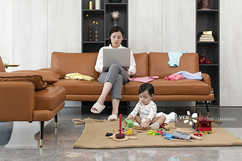 年轻妈妈在家忙工作而忽略宝宝图片素材