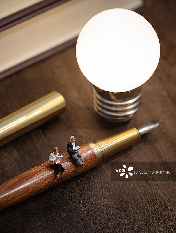 微缩创意暖色系书本木桌上灯泡钢笔上阅读的人图片素材