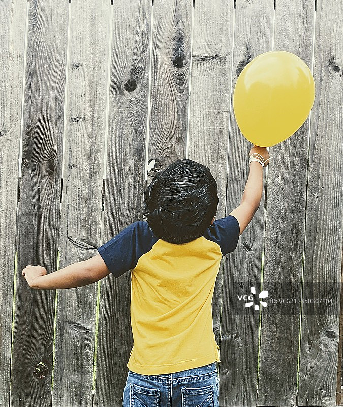 男孩靠墙拿着气球的背影图片素材