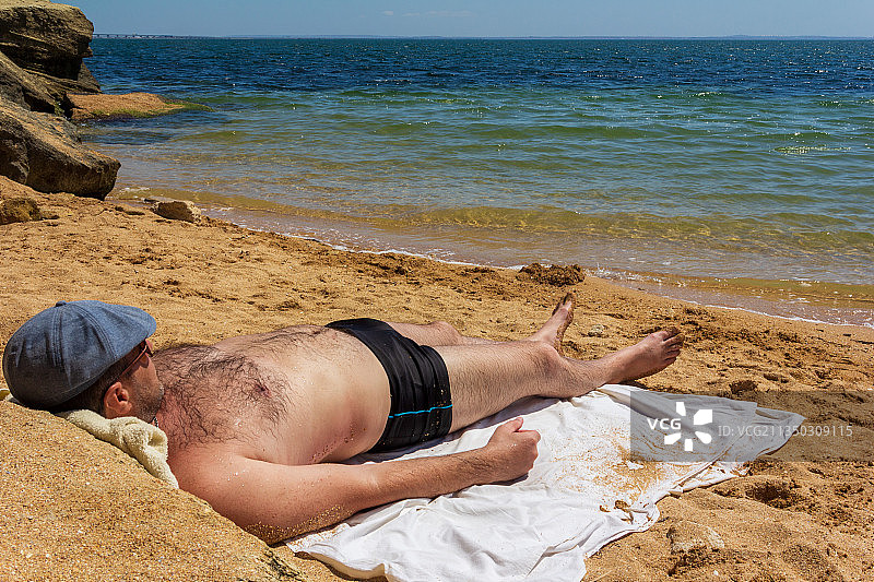 男人躺在海滩的沙滩上，以天空为背景图片素材
