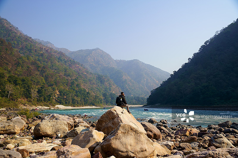 男人坐在印度北阿坎德邦瑞诗凯诗海滩的岩石上，眺望天空图片素材