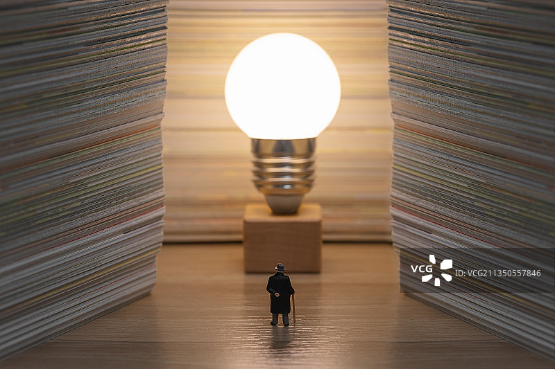 微缩创意堆叠的书本发亮的灯泡和老教师图片素材