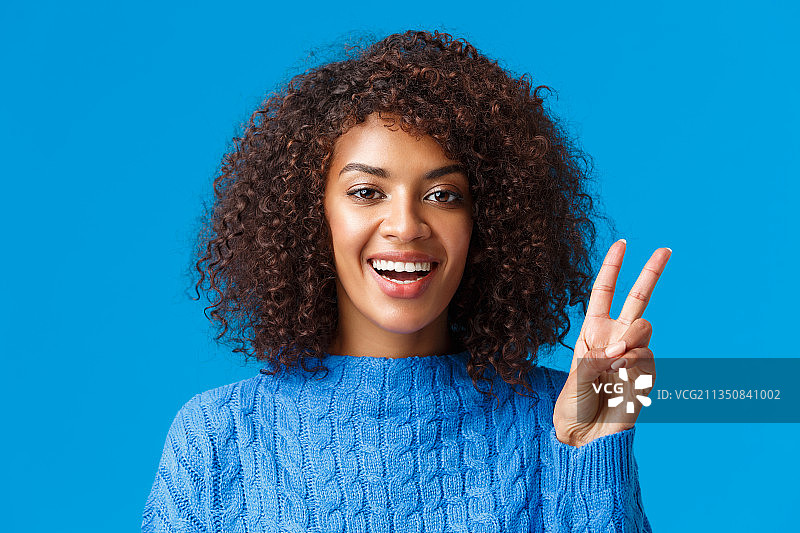 微笑的年轻女子手指放在嘴唇上，蓝色背景图片素材