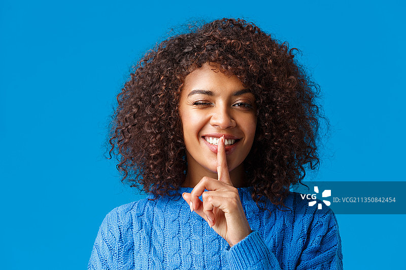微笑的年轻女子手指放在嘴唇上，蓝色背景图片素材