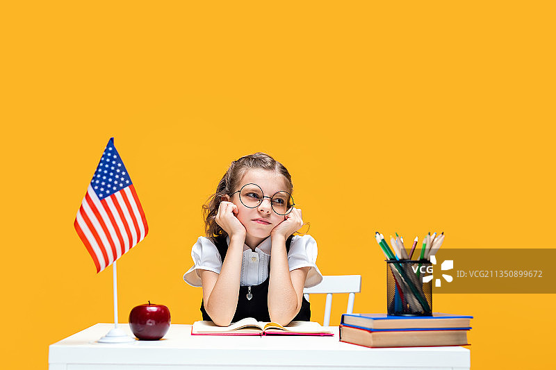 年轻的白人女学生坐在橙色背景的桌子旁图片素材