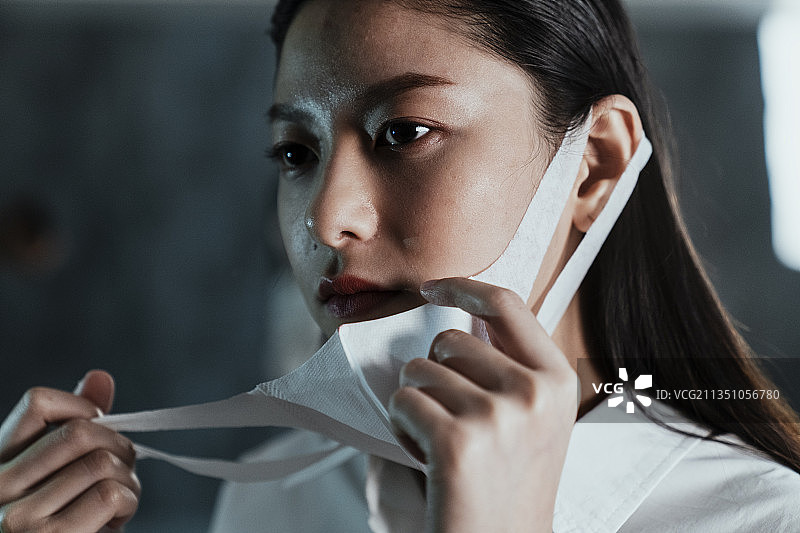 黑色长发女子摘下面具的特写镜头。图片素材