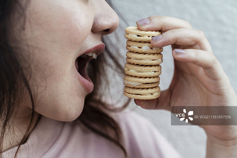 长发胖女人在白墙前试图同时吃六个饼干的特写镜头。图片素材