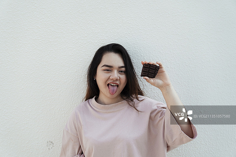 长头发的胖女人站在白墙上，手里拿着巧克力棒。图片素材