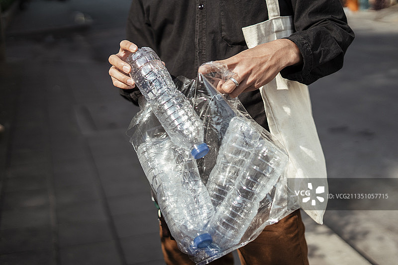 一名身穿黑衬衫的男子从人行道上收集了裁剪过的塑料瓶图像。图片素材
