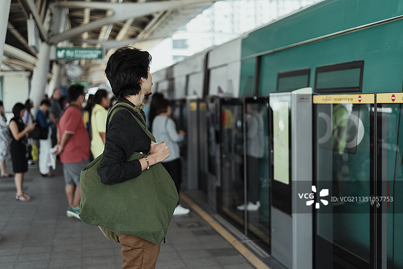 黑发男子平静地站在轻轨站，看着其他人试图进入列车。图片素材