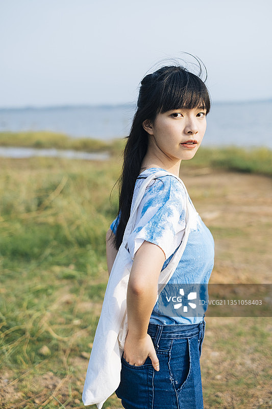 黑色半扎发髻的女孩穿着白色和蓝色的扎染的领带站在海边的草原上，拿着帆布包，偷她的后口袋。图片素材