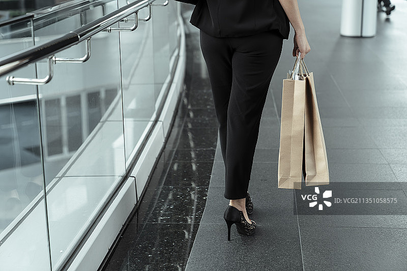 女商人的腿提着购物袋走在城市里。图片素材