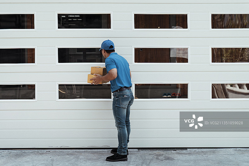 蓝色顾客送包裹的人站在房子门口。图片素材