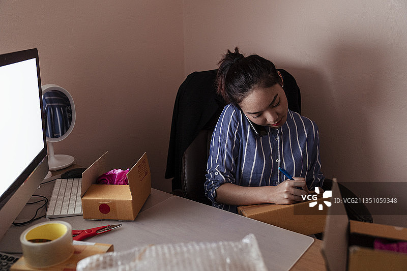 忙碌的亚洲泰国女人写地址纸箱和电话与客户。复制计算机空间。图片素材