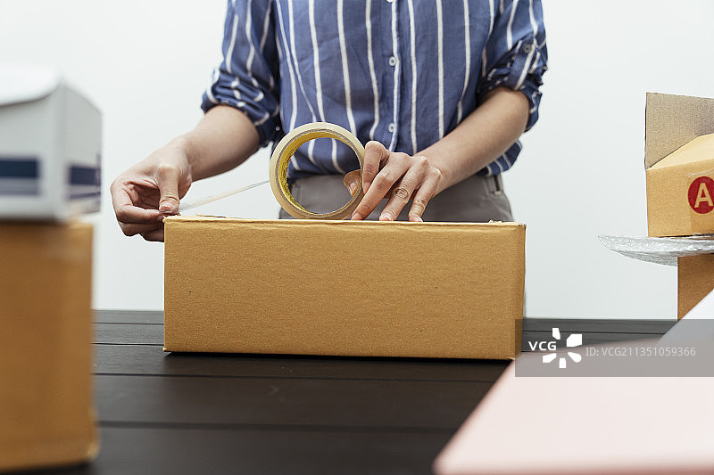 女手包装运输箱透明胶带在桌上。图片素材