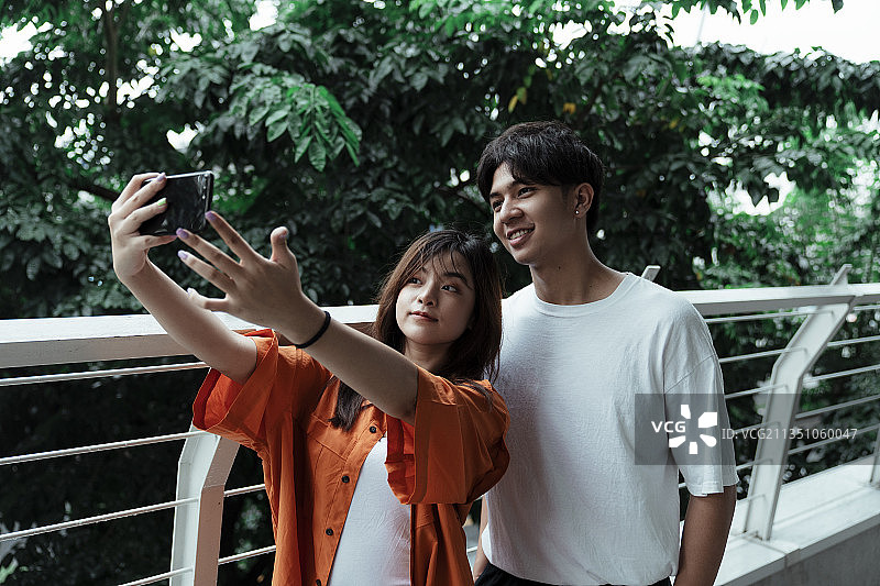 一对十几岁的情侣站在树旁的露台上一起自拍。图片素材