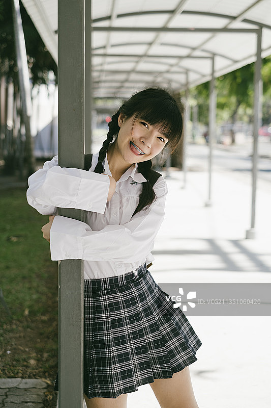 扎着马尾辫、留着刘海的女学生拥抱着小路的柱子。图片素材