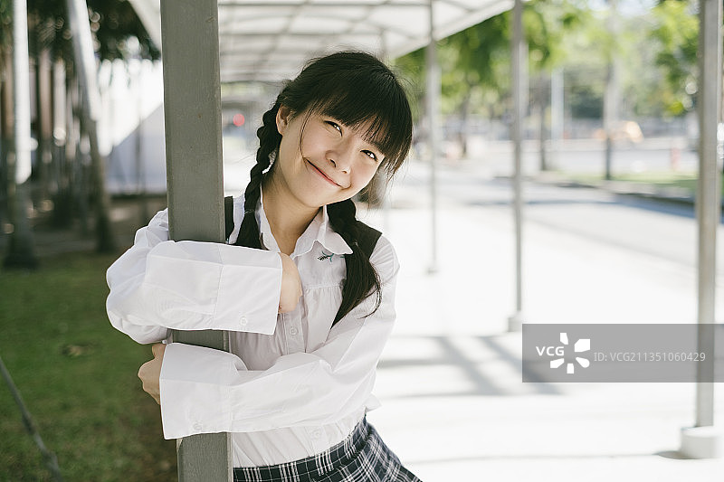 扎着马尾辫、留着刘海的女学生拥抱着小路的柱子。图片素材