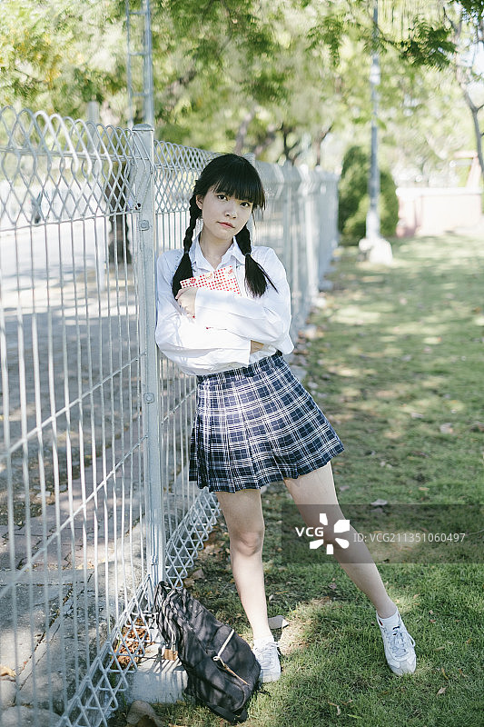 扎着马尾辫和刘海的女学生抱着书把身体倾斜到栅栏上。图片素材