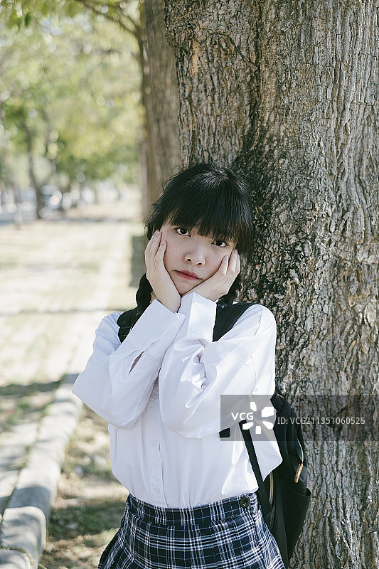 扎着马尾辫、留着刘海的女学生在树下摸着她的脸颊。图片素材