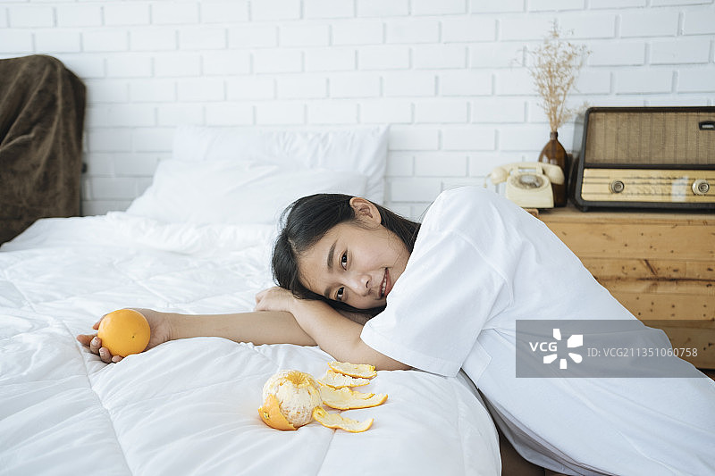 可爱的年轻亚洲女人与橙色水果在卧室。健康的概念。图片素材
