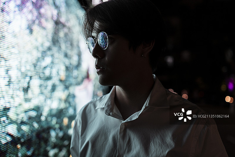 水平拍摄的黑头发的家伙，穿着白衬衫，戴着眼镜，站在商场的LED广告牌，他停止了行走，因为对LED显示感兴趣。图片素材