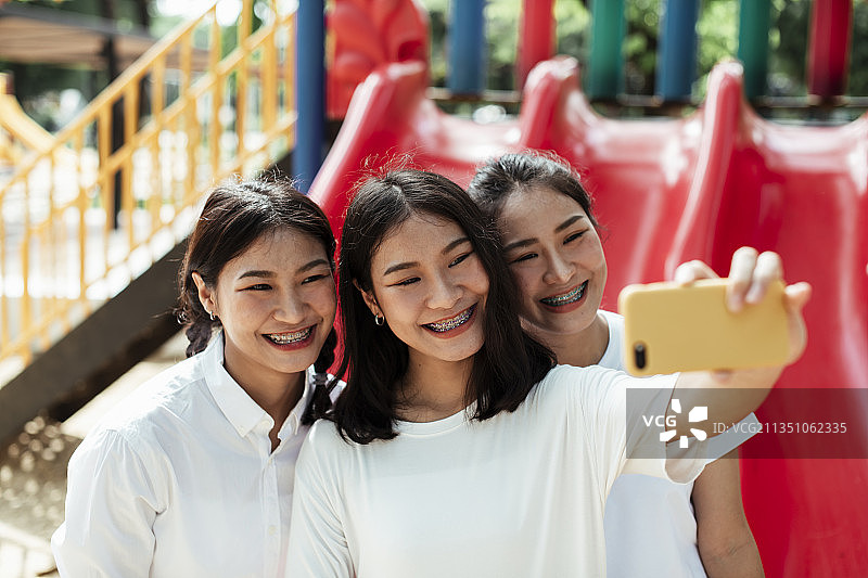 三胞胎姐妹在公园操场的红色滑块末端自拍。图片素材