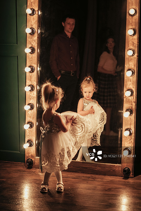 穿着漂亮裙子的俄罗斯小女孩站在镜子前图片素材