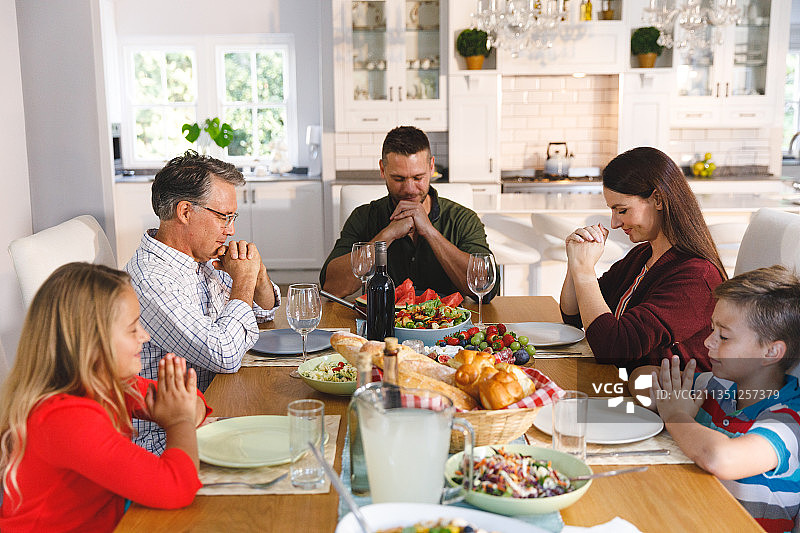白人祖父、父母与儿子和女儿在餐桌旁，饭前祈祷图片素材