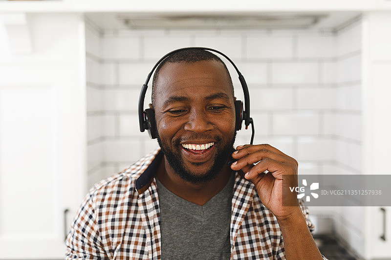 坐在厨房台面上，戴着耳机进行视频通话的非裔美国人男子图片素材